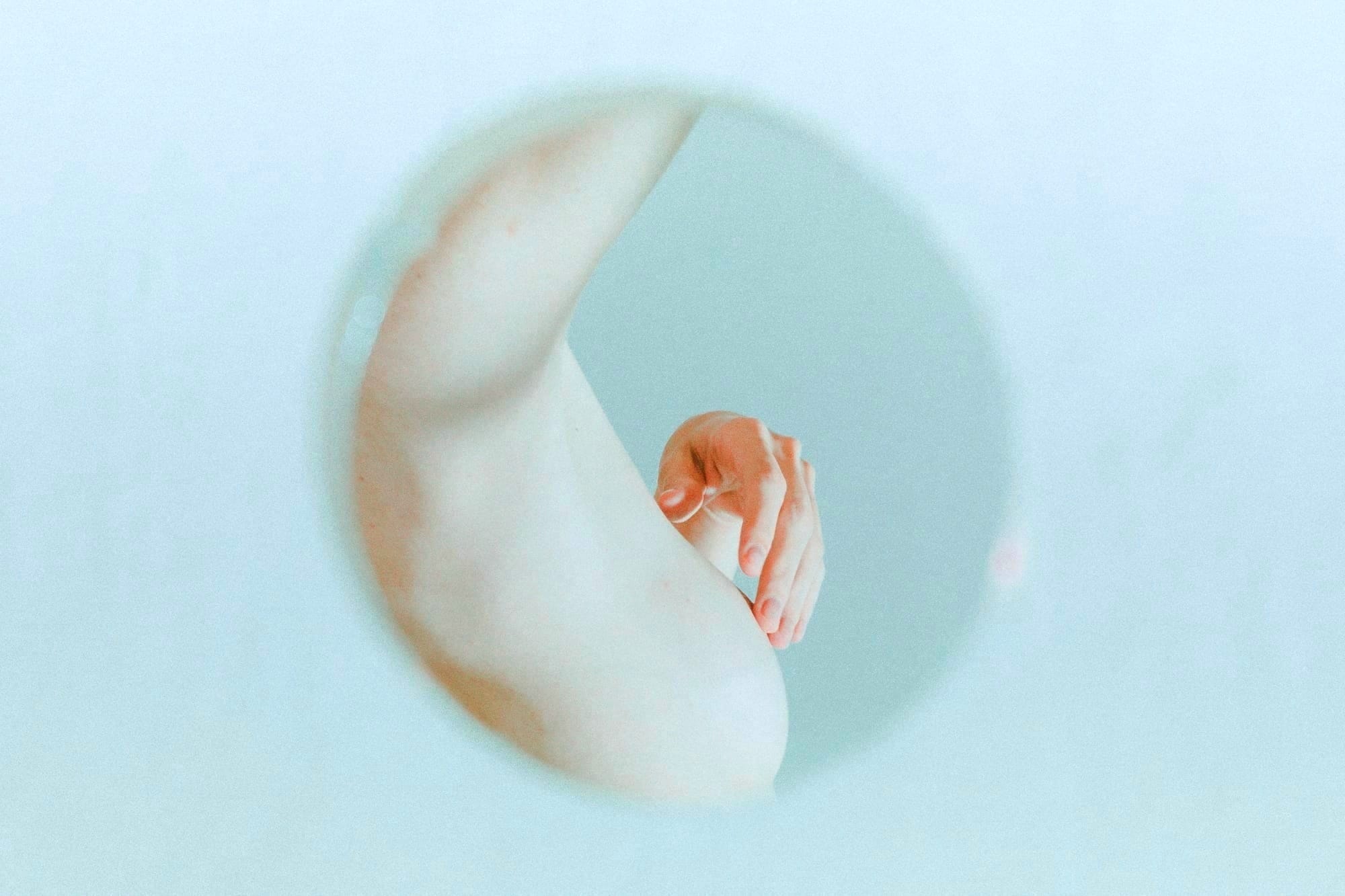 a nude woman's partial reflection in a circular mirror