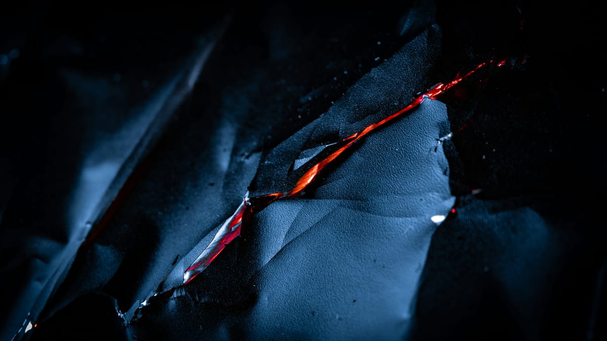 A close-up of a sheet of dark, sharp metal sliced thinly in the center.