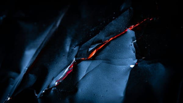 A close-up of a sheet of dark, sharp metal sliced thinly in the center.