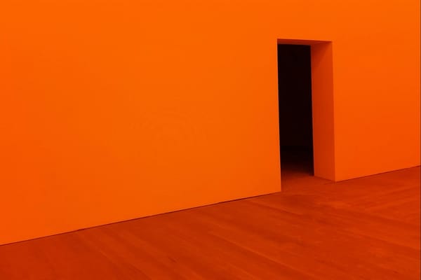 A wooden floor and a bright orange wall with an opening for a door, revealing nothing but darkness.